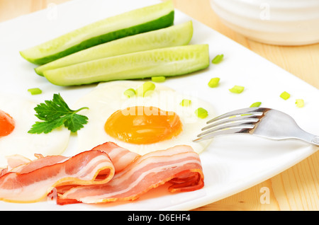 Frühstück mit Speck, Spiegelei und Scheiben Gurke auf weißen Teller Stockfoto