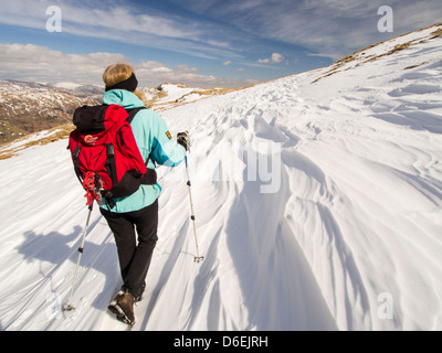 Sastrugi verursacht durch Wind Scour auf der Schneedecke über dem Wrynose Pass im Lake District, Großbritannien mit einer Frau Walker. Stockfoto