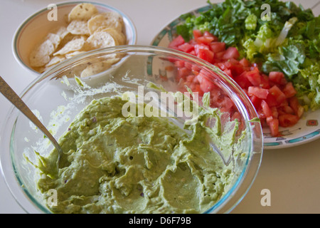 Nahaufnahme einer Schüssel voller Frische Guacamole neben Schalen bunt gehackten Salat, Tomaten und Mais-chips Stockfoto