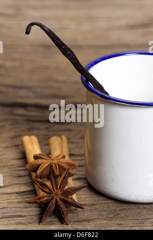 Zimt-sticks, Sternanis und Vanilleschote in einer Emaille-Tasse auf rustikalem Holzbrett Stockfoto