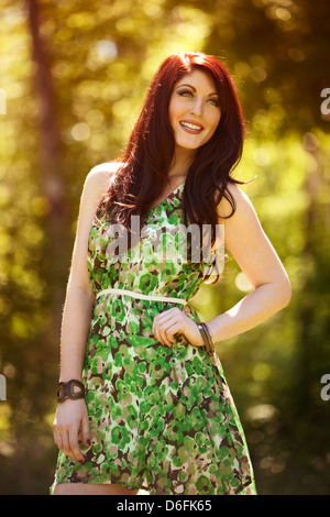 Frau in Grün Blume Kleid vor Bäumen draußen Stockfoto