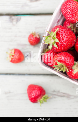 Ein Karton voller Reife rote Erdbeeren, auf eine leicht verwitterte Holzbank Stockfoto