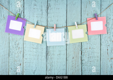 Fünf leere bunte Bilder oder Notizen Fotopapier mit Wäscheklammern aus Holz blau Vintage shabby-chic Hintergrund hängen Stockfoto