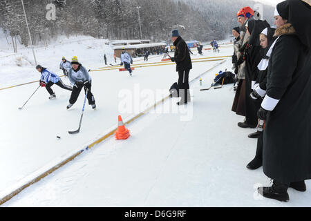 Teilnehmer des zweiten DEB Pond Hockey Cup sind in Aktion, abgebildet, während drei Nonnen auf dem zugefrorenen Riesser See in Garmisch-Partenkirchen, Deutschland, 12. Februar 2012 anschauen. Amateure und professionelle Eishockey-Spieler nahmen Teil in das geschehen. Foto: Andreas Gebert Stockfoto