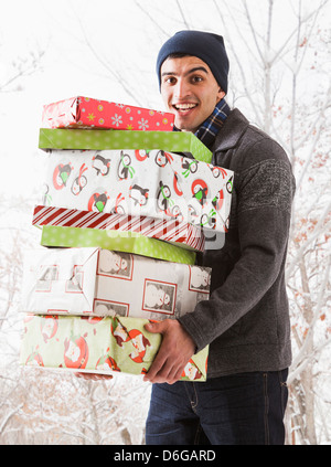 Hispanic Mann hält Weihnachtsgeschenke im Schnee Stockfoto