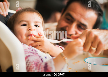 Hispanische Vater Tochter im Hochstuhl füttern Stockfoto
