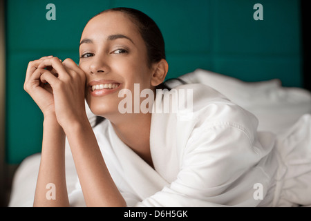 Frau im Bademantel lächelnd auf Bett Stockfoto