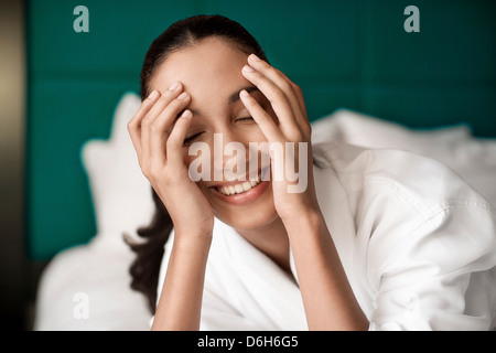 Frau im Bademantel lächelnd auf Bett Stockfoto