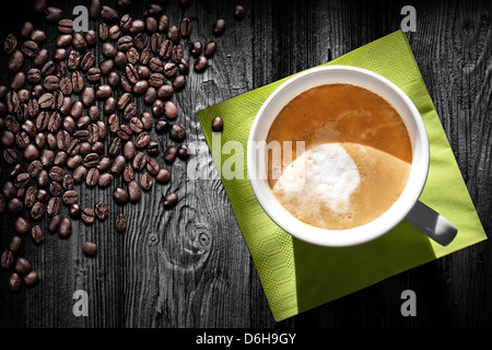 Tasse Cappuccino Kaffee, grünen Serviette und Bohnen auf schwarzer Holztisch, Ansicht von oben Stockfoto