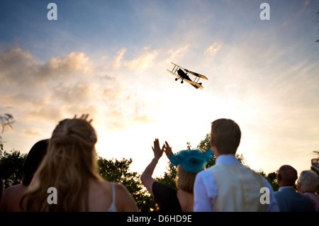 Im späten Sommernachtsabend einer Hochzeitsfeier fliegen Doppeldecker über Hochzeitsgäste hinweg Stockfoto