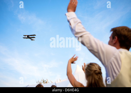 Biplane fliegt als Hochzeitsgeschenk für Braut und Bräutigam an Hochzeitsgästen vorbei Stockfoto