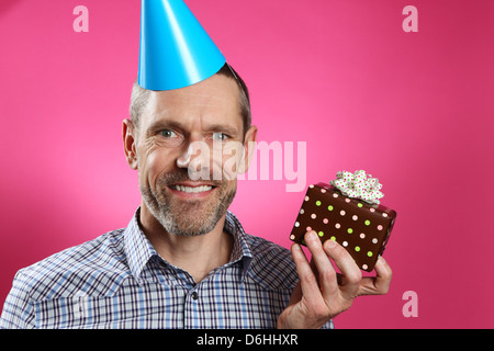 Mann trägt einen Partyhut mit einem toothy Lächeln und hält ein Geschenk. Stockfoto