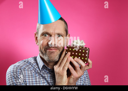 Mann mit Partyhut, lächelnd und hält ein Geschenk in der Nähe von seinem Gesicht. Stockfoto