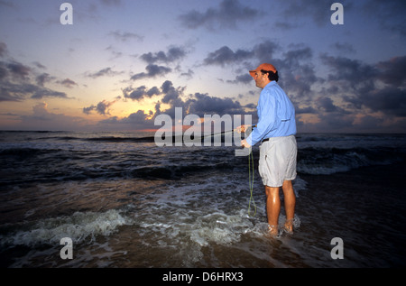 Ein Angler Fliegenfischen in der Brandung vom Strand bei Sonnenaufgang für Rotbarsch an neuen Smyrna Florida Stockfoto