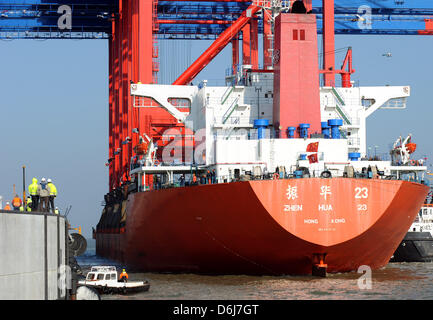 Ein Frachtschiff mit riesigen Containerbrücken beladen kommt an der Pier des JadeWeserPort in Wilhelmshaven, Deutschland, 6. März 2012. Vier neue neue Portalkräne haben endlich nach dem Versand für zwei Monate an Bord die 245 Meter lange "Zhenhua 23' aus China. Die Krane sind für den Eurogate Container Terminal, dem neuen Tiefwasser-Hafen bestimmt. Die Krane markieren die erste arriva Stockfoto