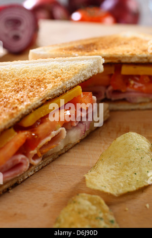 Nahaufnahme von geröstetem Schinken Käse Tomate Sandwich mit Chips auf einem hölzernen Steckbrett Stockfoto