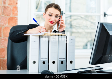 Junge Geschäftsfrau arbeiten in ihrem Büro, sie sitzt hinter Ordner und am Telefon ist ein Kunde oder Klient Stockfoto