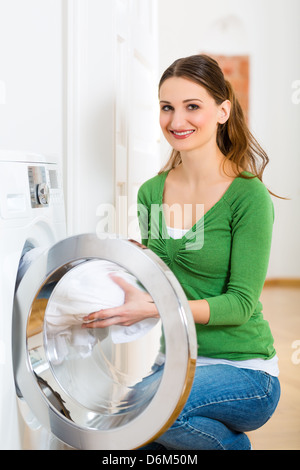 Junge Frau oder Haushälterin hat Waschtag zu Hause, sie nimmt sich die, die Waschmaschine oder den Trockner Stockfoto