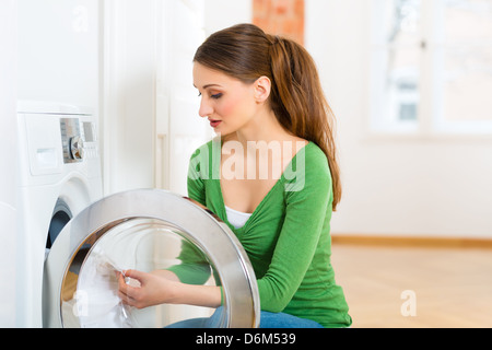 Junge Frau oder Haushälterin hat Waschtag zu Hause, sie nimmt sich die, die Waschmaschine oder den Trockner Stockfoto