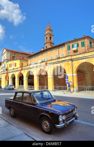 Alte schwarze Auto steht auf der Straße vor gelben gewölbten Durchgang und rotem Backstein Glockenturm unter blauem Himmel in Stadt Bra, Italien. Stockfoto