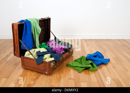 Leder-Koffer auf einen Holzboden in einem leeren Raum, voll von bunten Kleidung. Stockfoto