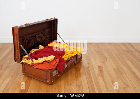Leder-Koffer auf dem Holzboden, voll von orange, rote und gelbe Kleidung. Stockfoto