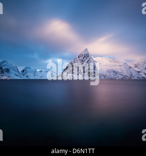 Winter-Sonnenaufgang auf Schnee bedeckt Olstind Mountain Peak steigt aus Toppøya, Moskenesøy, Fjord, Lofoten Inseln, Norwegen Stockfoto