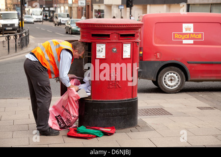 Ein Royal Mail Postbote UK Entleerung e-Mails aus einer Mailbox, mit seinem roten Royal Mail van, York, Yorkshire UK Stockfoto
