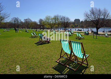 Liegestühle mit The Serpentine im Frühjahr, Hyde Park, City of Westminster, London, Greater London, England, Vereinigtes Königreich Stockfoto