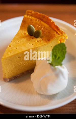 Kürbis (oder Squash) Käsekuchen serviert mit Sahne und garniert mit Kürbiskernen auf einem weißen Teller. Stockfoto