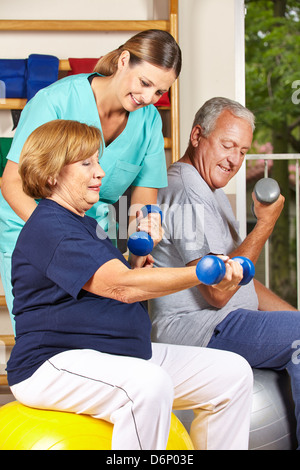 Zwei ältere Leute tun Hantel Fitnesstraining mit Physiotherapeuten Stockfoto