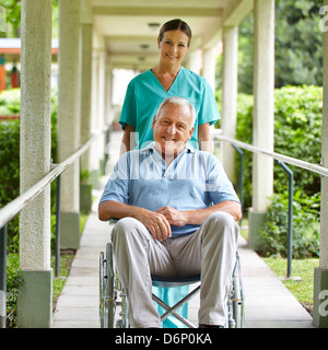 Glücklich Krankenschwester Schieben Rollstuhl mit senior Mann im Krankenhaus Garten Stockfoto
