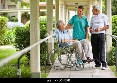 Zwei Seniorinnen und Senioren im Gespräch mit einer Krankenschwester in einem Krankenhaus-Garten Stockfoto