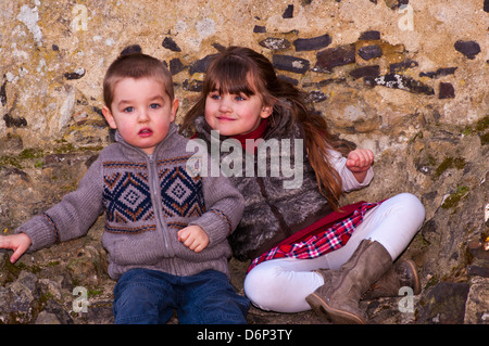 Young Bruder und Schwester gekleidet In warme Kleidung gemeinsam draußen sitzen Stockfoto