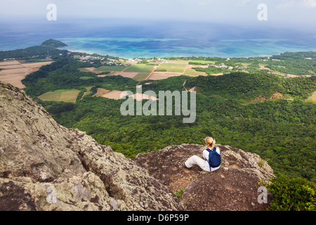 Eine Frau sitzt und bewundert die Küste Aussicht von der Spitze des Mount Nosoko in Ishigaki, Okinawa, Japan Stockfoto