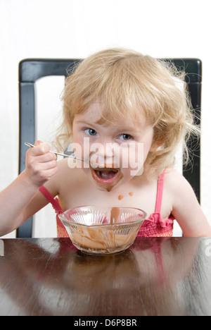 Junge Mädchen am Tisch einen Schokoladenpudding Essen bekommt mehr chaotisch: Studioportrait isoliert auf weiss Stockfoto