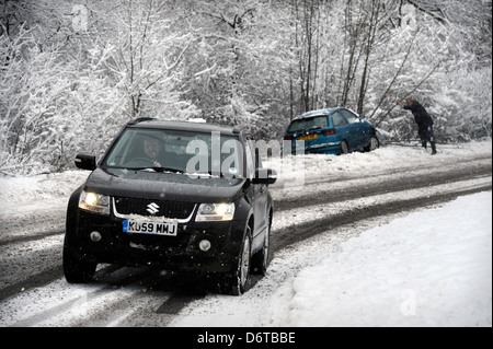 Ein 4 x 4 Fahrzeug fährt ein abgestürztes Auto, das die Strasse in den schneebedeckten Bedingungen in der Nähe von Stroud Gloucestershire UK links Stockfoto