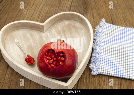 Ein Granatapfel mit einer herzförmigen Schnitt und einen Löffel mit Samen auf einem Holztablett Stockfoto