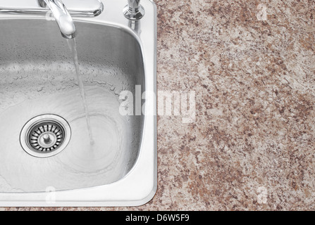 Wasser läuft aus der Küchenarmatur. Saubere neue Spüle und Arbeitsplatte Detail. Stockfoto