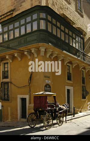 Ein barouche Pferdekutsche fahren Sie unter einer Ecke Balkon aus Holz in Valletta, die Hauptstadt von Malta Insel gezeichnet Stockfoto