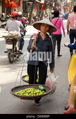 Vertikale Porträt einer vietnamesischen Dame tragen Körbe Äpfel auf einem Bambus-Schulterstütze durch die Altstadt in Hanoi. Stockfoto