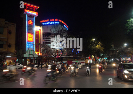 Horizontale Nightscape das äußere des berühmten Thang Long Wasser Puppentheaters in Hanoi mit Verkehr fahren übergeben. Stockfoto