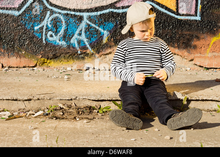 Schmollen, kleiner Junge auf einem Bürgersteig in der Sonne trägt eine Baseballkappe, wandte sich an die Seite mit einem mürrischen schmollendes Ausdruck auf seinem Gesicht sitzt. Stockfoto