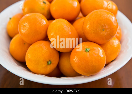 Clementinen, Orangen, eine Vielzahl von Mandarine, Citrus reticulata, in einer weißen Schüssel, sitzen auf einem hölzernen Tisch. Nahaufnahme. Stockfoto