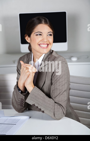 Attraktive Geschäftsfrau, die lächelnd in ihrem Büro an einem Tisch Stockfoto