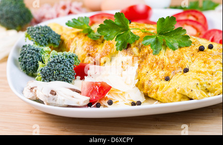 Horizontale Foto großes Ei Omelett mit Champignons, Käse, Broccoli, Tomatenscheiben, Pfeffer und Petersilie in weißer Teller Stockfoto