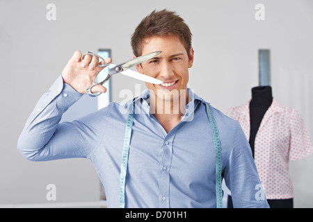 Mann im Studio Holding eine Schneiderin Scheren vor seinem Gesicht lächelnd Stockfoto