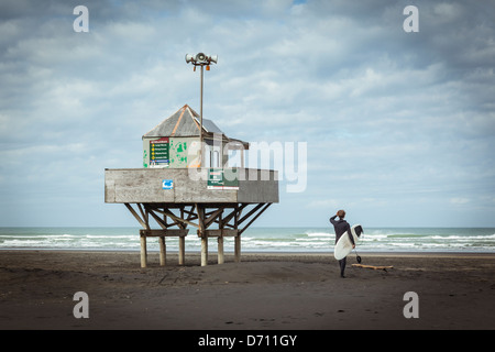 Eine Surfer steht neben der Bademeister Aussichtsturm am Bethells Strand (Te Henga) auf Aucklands Westküste, New Zealand. Stockfoto