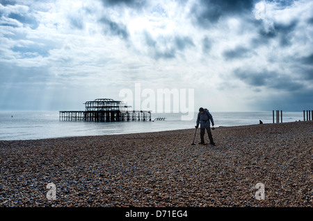 Ein Mann verwendet einen Metalldetektor auf Brighton Beach auf front ot die Ruine der West Pier. Stockfoto