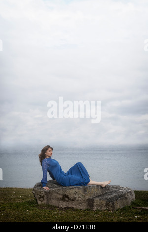 eine Mädchen in einem blauen Kleid ist auf einem Stein liegen. Stockfoto